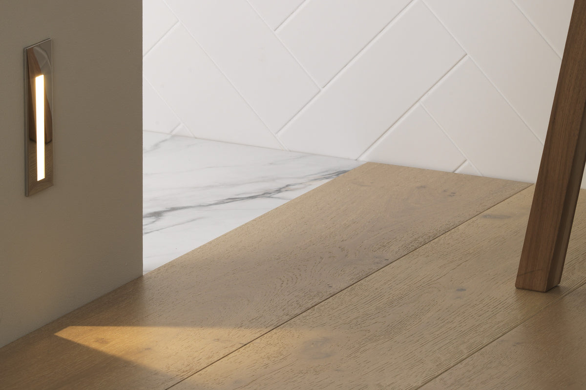 Light fixture on a wall next to a wooden floor with a chair leg partially visible.