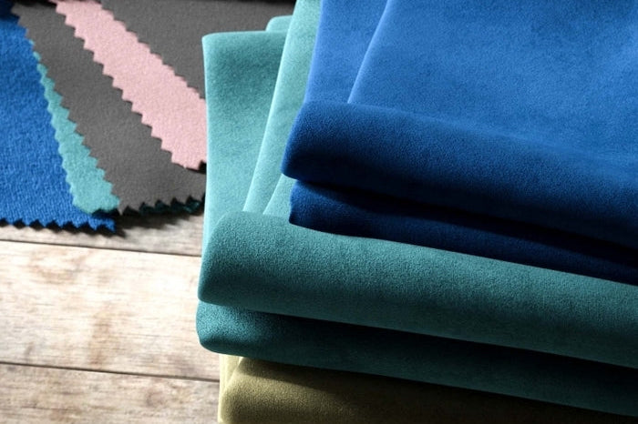 Stack of folded velvet fabric swatches in various colors on a wooden surface.
