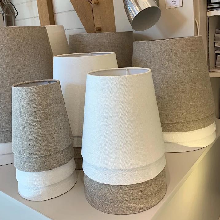 A collection of natural linen lamp shades displayed, showing a range of sizes from small to large with a two-tone color design.