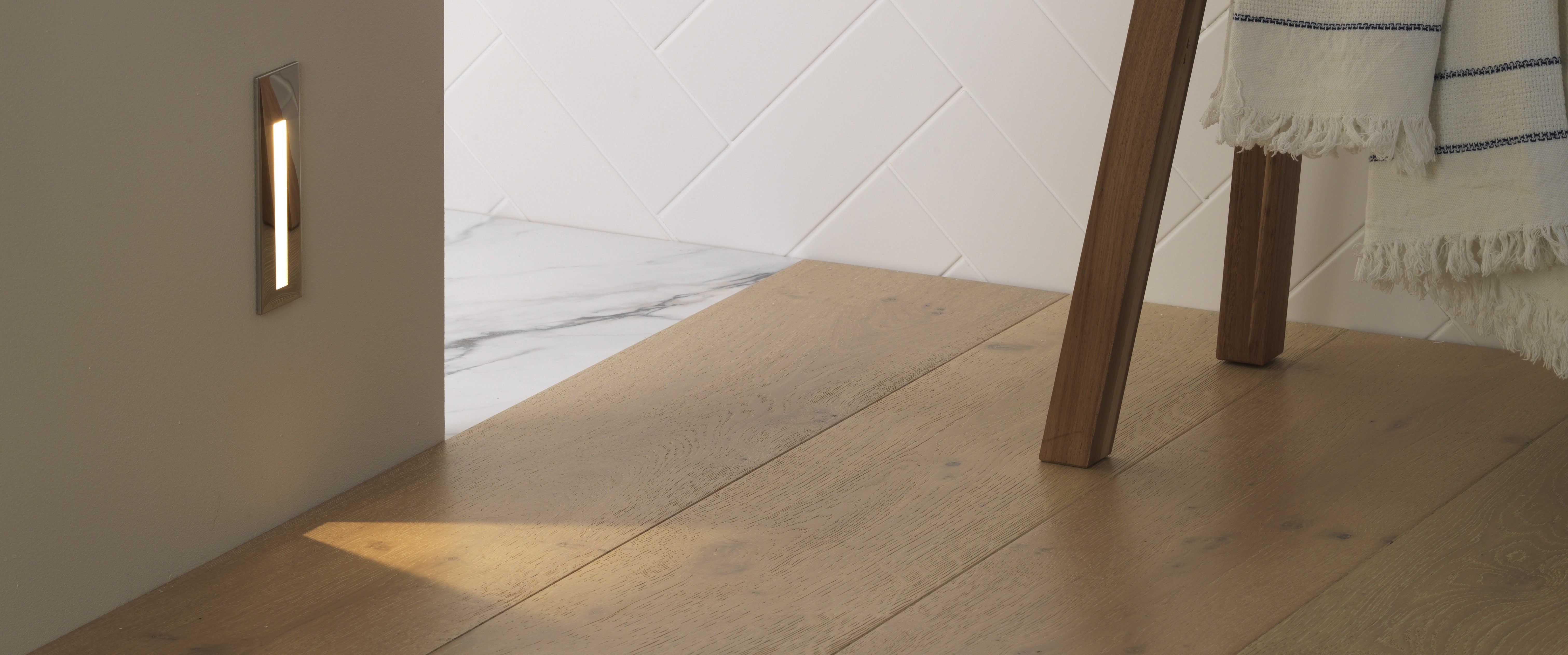 Light fixture on a wall next to a wooden floor with a chair leg partially visible.